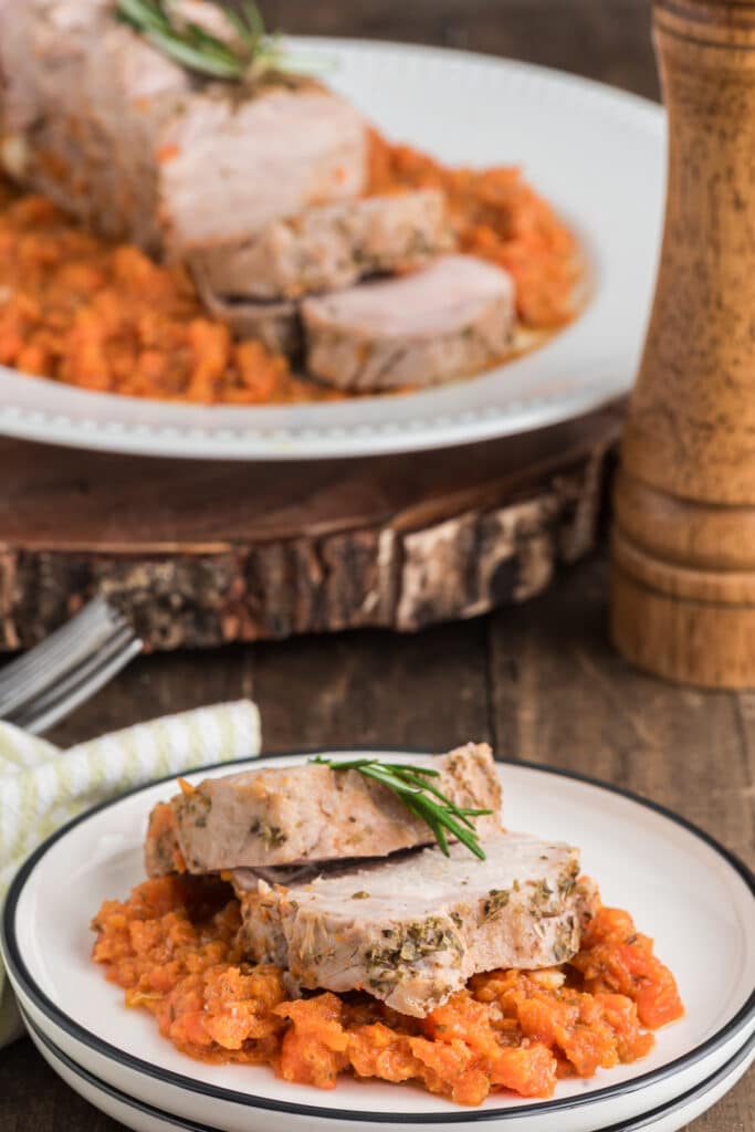Pork roast on a plate with carrots and two slices on a white plate.