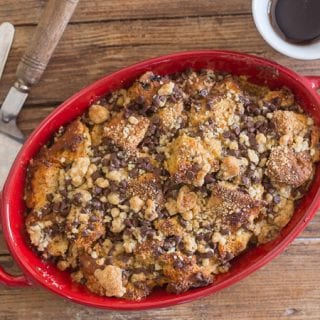 baked panettone french toast casserole in a red baking dish with a spatula and a fork on a wooden board