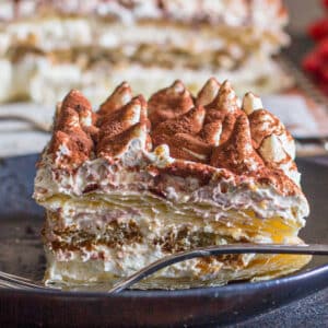 A slice of tiramisu on a black plate.