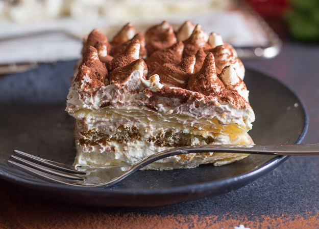 up close puff pastry tiramisu on a black plate.