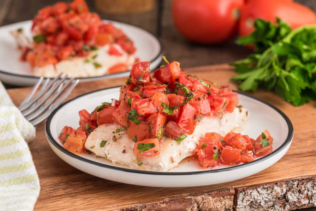 Baked fish marinara on a white plate.