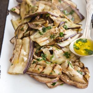 grilled eggplant on a white pan with a brass spoon