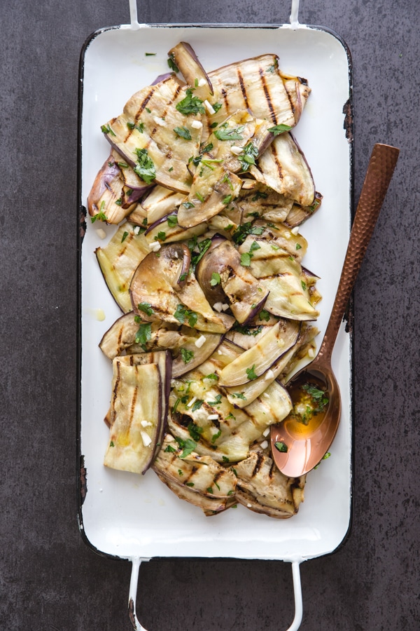 grilled eggplant on a white pan with a brass spoon