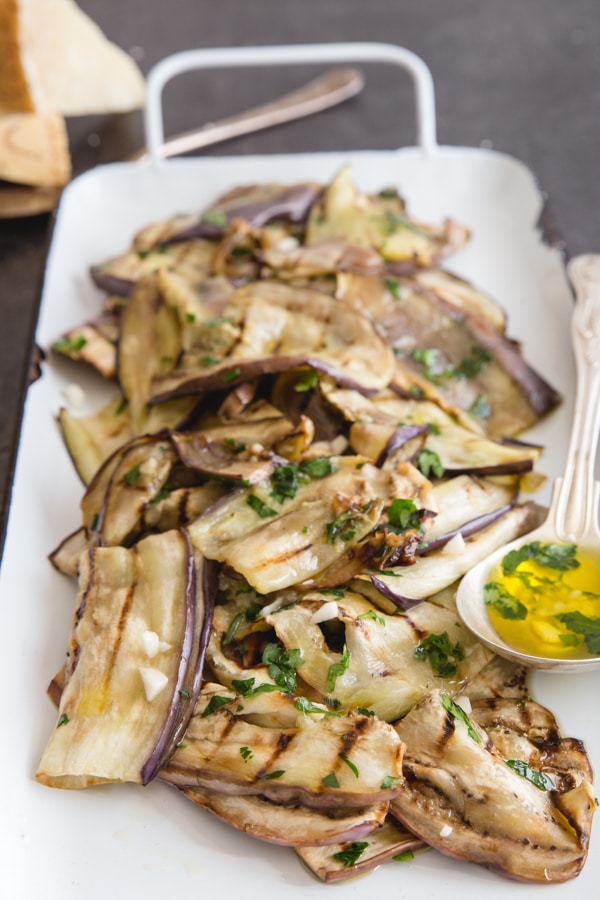 grilled eggplant on a white pan with a brass spoon