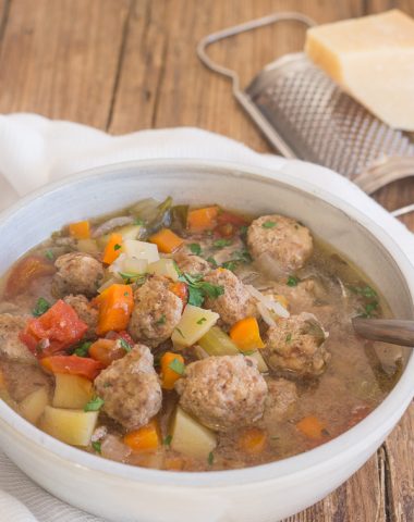 Italian meatball soup on a wooden board in a white bowl with a soup