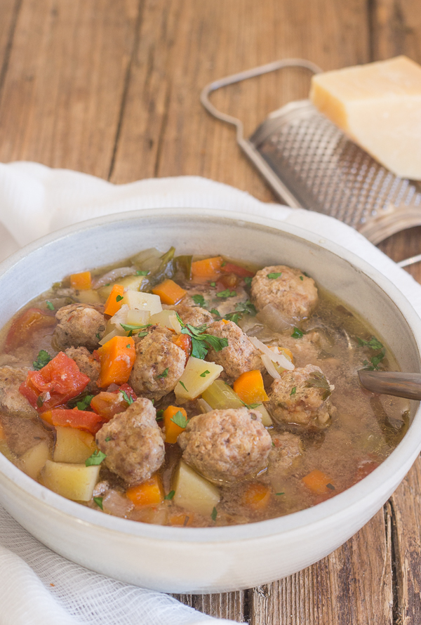 Italian meatball soup on a wooden board in a white bowl with a soup