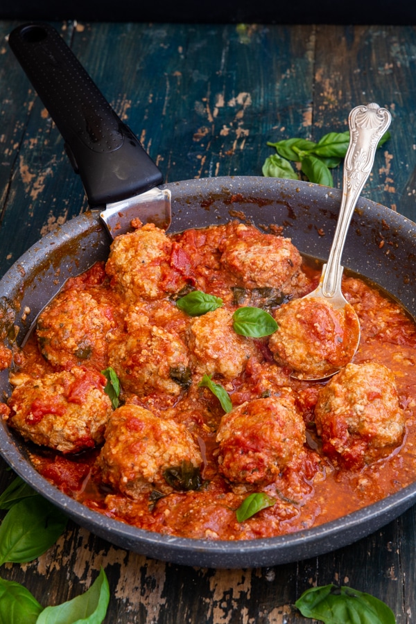 meatballs in a black pan with a silver spoon