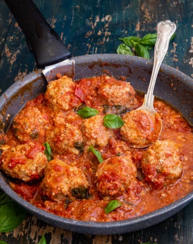 meatballs in a black pan with a silver spoon