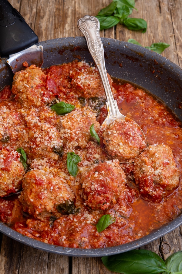 meatballs cooked in a black pan with a silver spoon and sprinkled with parmesan cheese