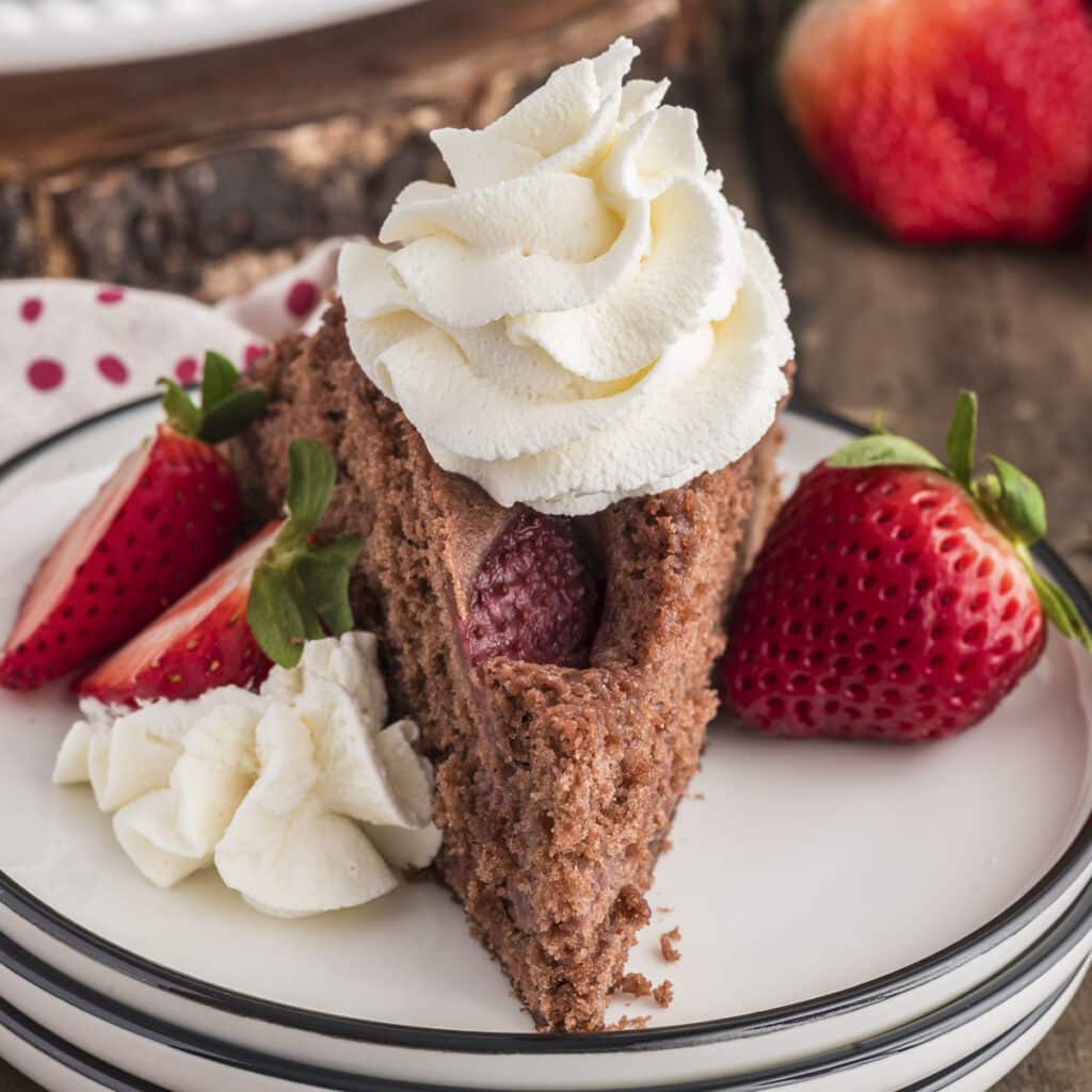 A slice of strawberry cake on a white plate with whipped cream.