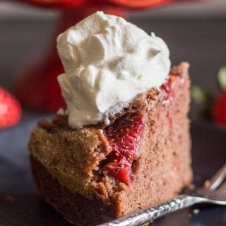 a slice of chocolate strawberry cake on a black plate with whipped cream on top