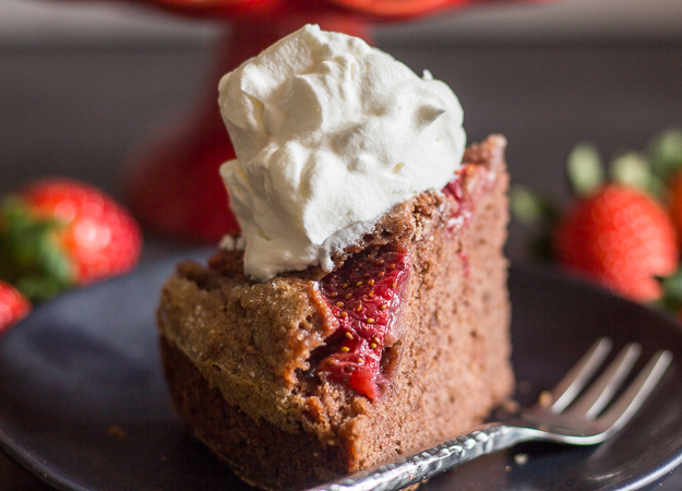 a slice of chocolate strawberry cake on a black plate with whipped cream on top