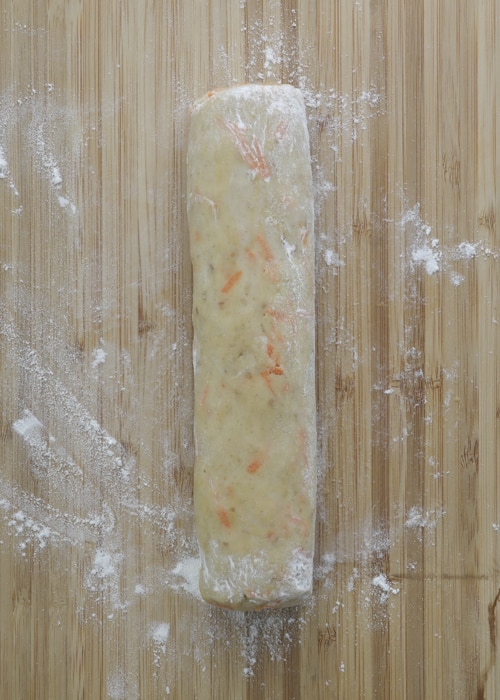 The dough formed into a log and on plastic wrap on a wooden board.