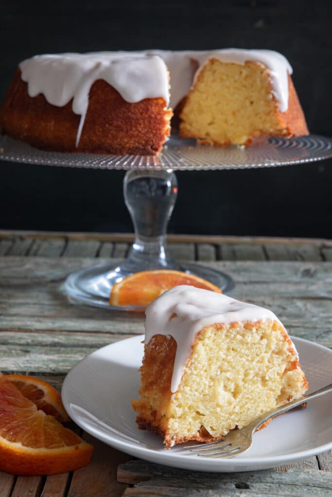 Orange cake on a glass cake dish with a slice on a white plate.