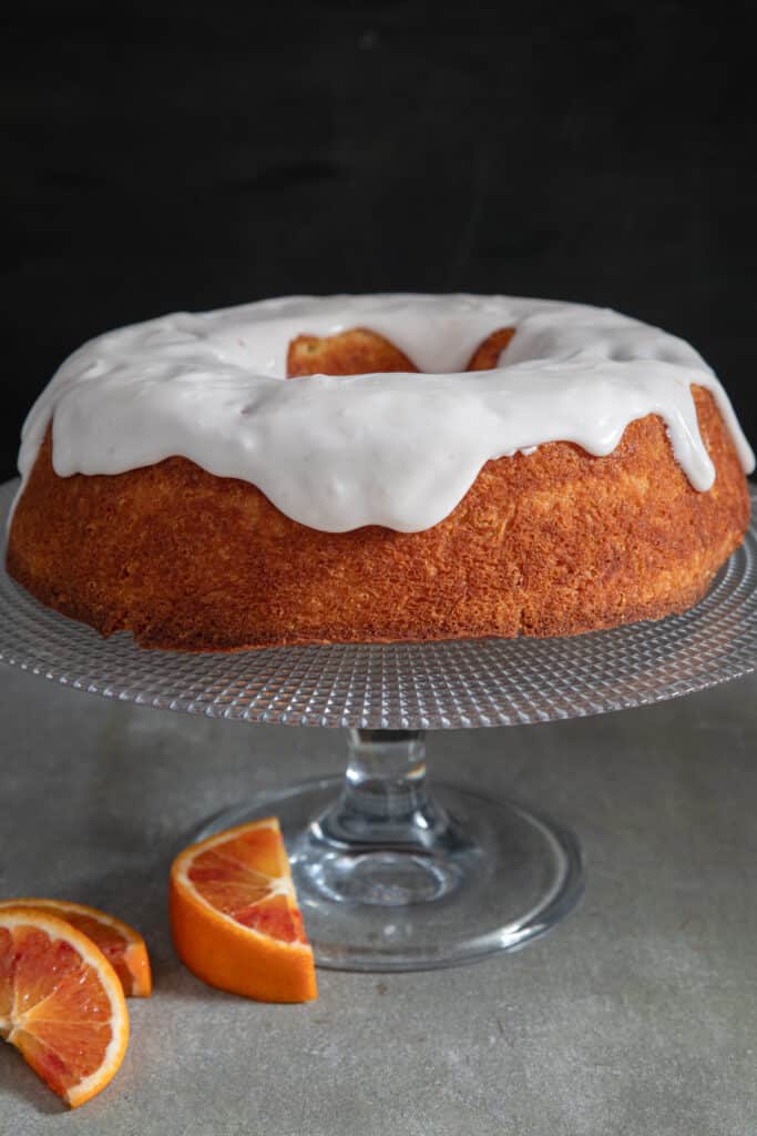 Simple glazed orange cake on a glass cake stand.