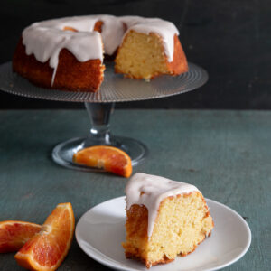 Orange cake on a glass cake dish with a slice on a white plate.