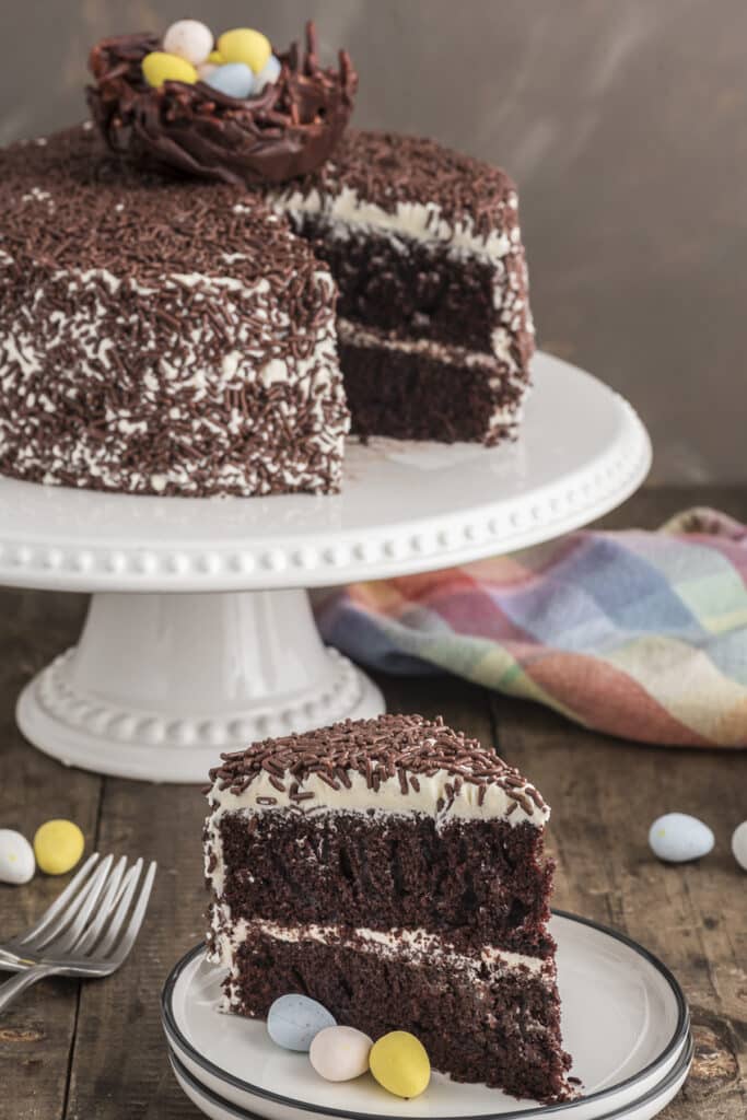 Chocolate cake on a cake stand with a slice on a white plate.