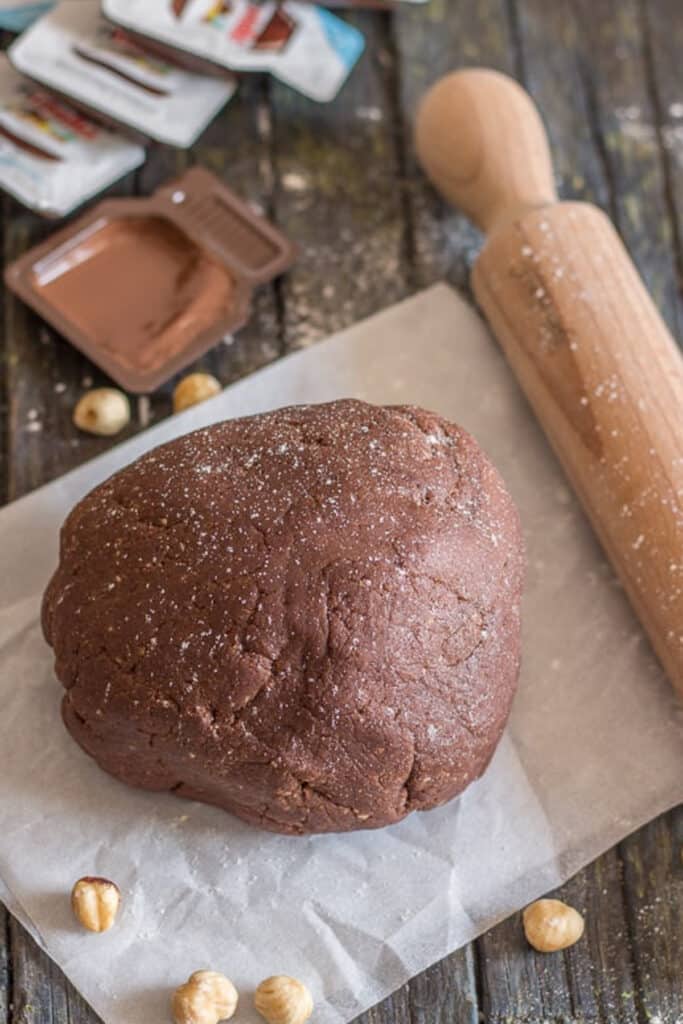 Pie dough on a waxed paper, with a rolling pin and hazelnuts.