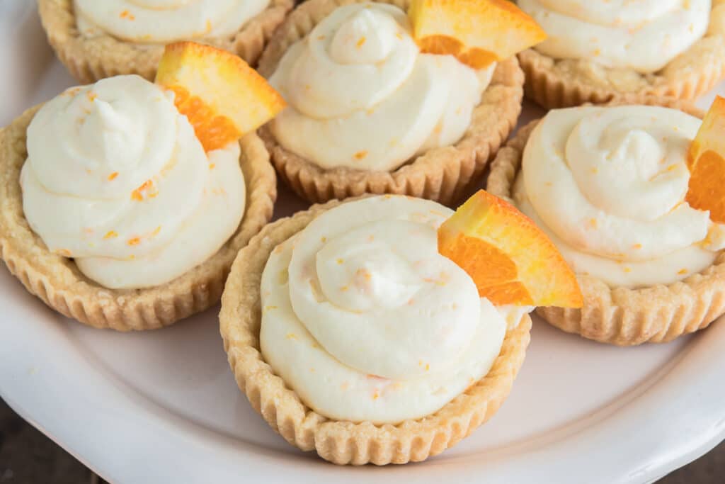 Orange cheesecake tarts on a white plate.