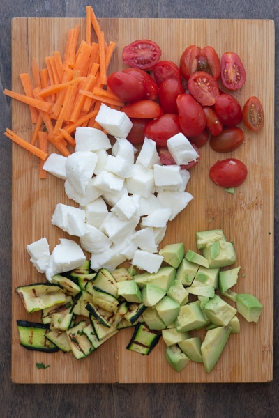 the cut up vegetables and cheese on a wooden board.
