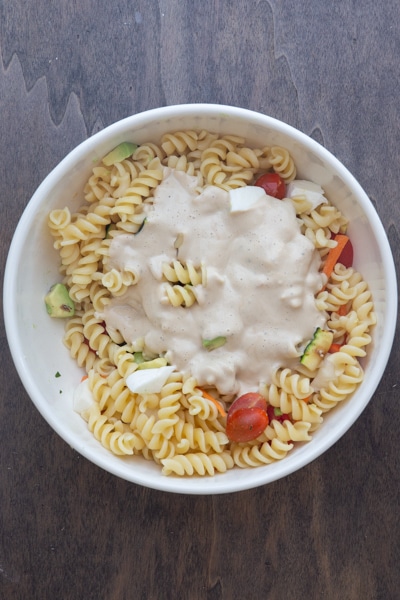 The pasta, dressing and vegetables in a white bowl.