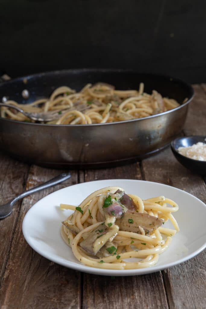 Eggplant bucatini in a pan and some on a white plate.