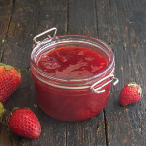 Jam in a jar with strawberries on the board around it.