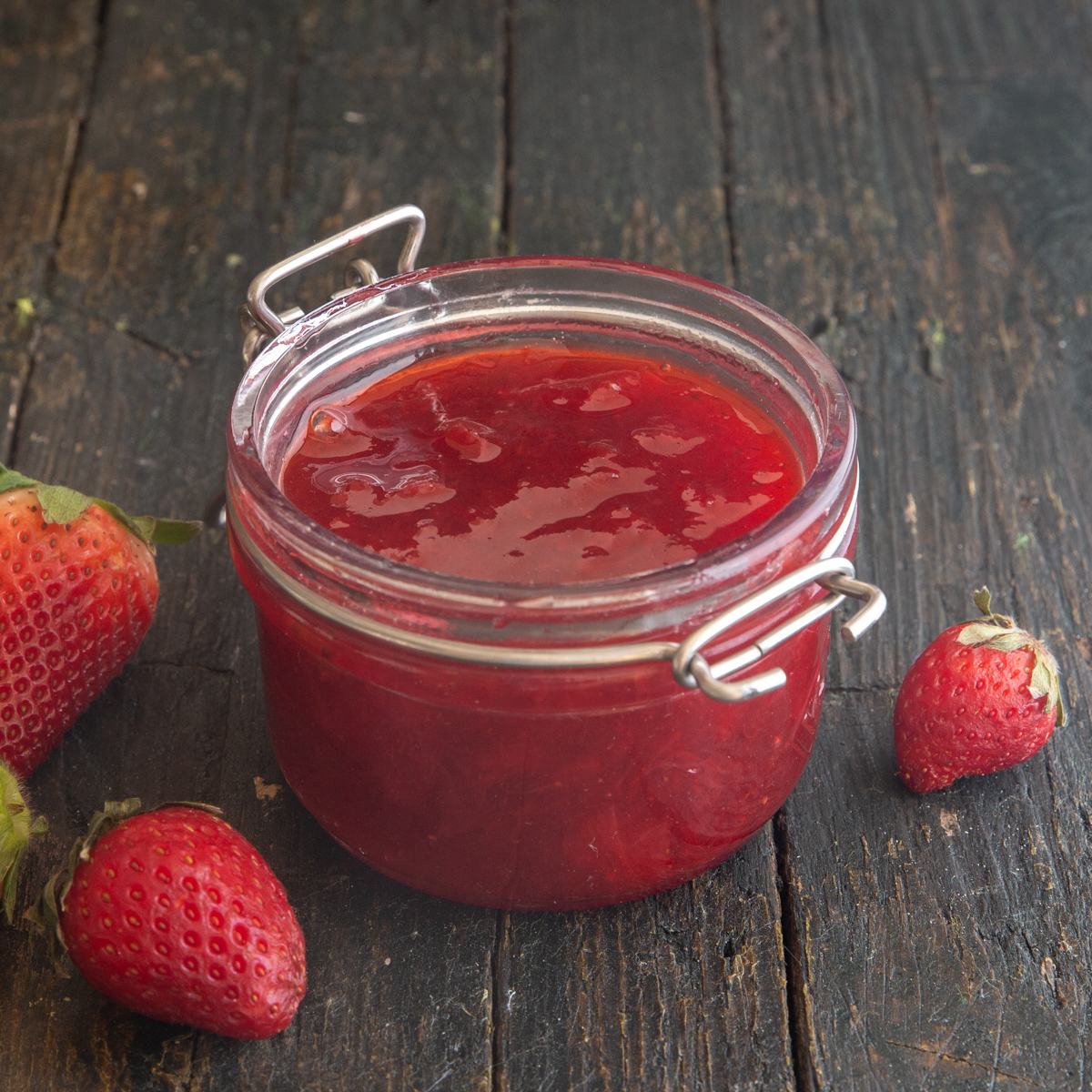 Jam in a jar with strawberries on the board around it.