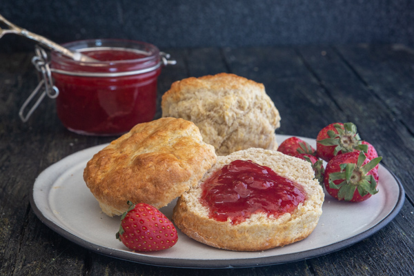 jam on a scone on a plate with jam in a jar.