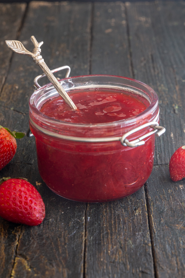 strawberry jam in glass jar with a spoon in it.