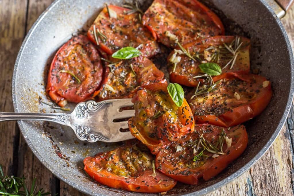 Fried tomatoes in a pan with a fork.