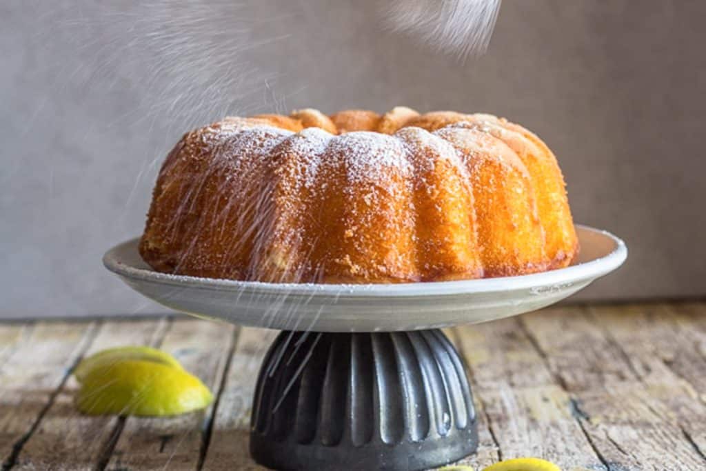 Lemon cake being dusted with powdered sugar.