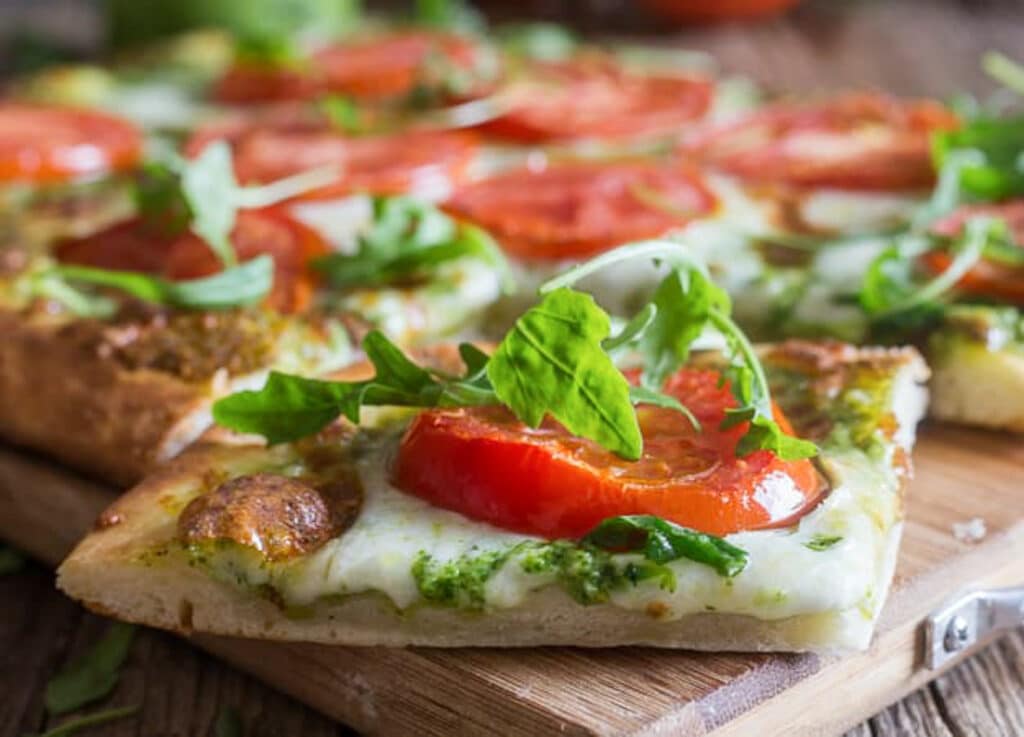 A slice of pesto pizza on a wooden board.