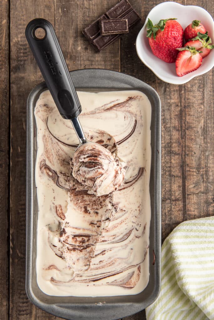 Ice cream in a loaf pan with a scoop and a dish of strawberries.