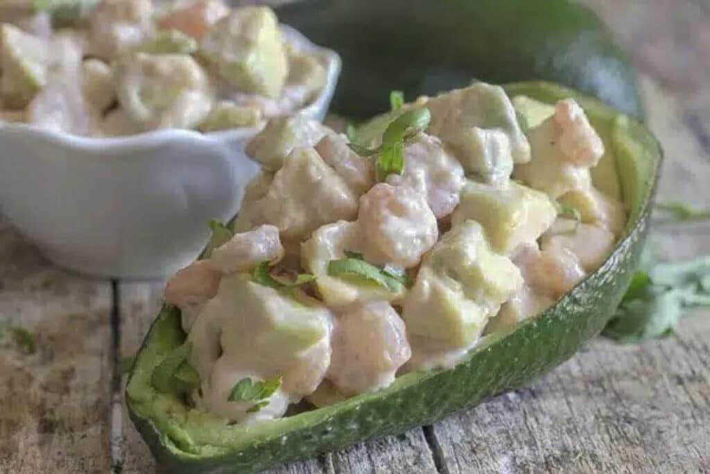 Stuffed avocado with filling in a white bowl.