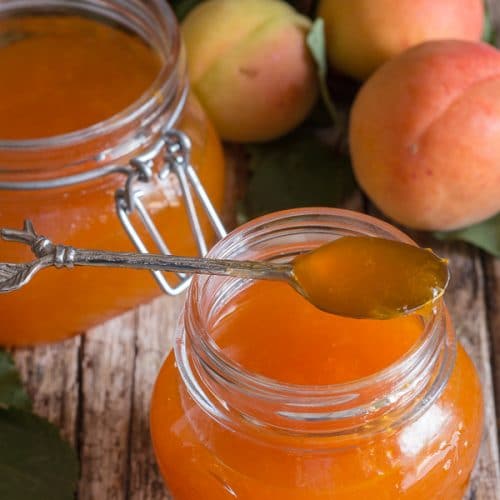 apricot jams in 2 jars with a spoonful of jam on the rim