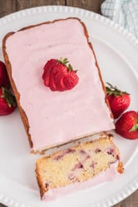 Strawberry cake with frosting on a white plate with a slice cut.