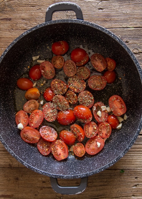 Tomatoes and spices in a black pan.