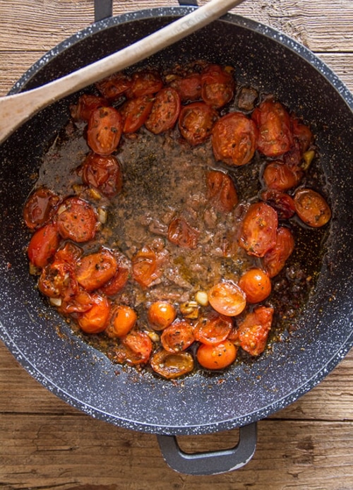 Tomatoes and anchovies cooked in a black pan.