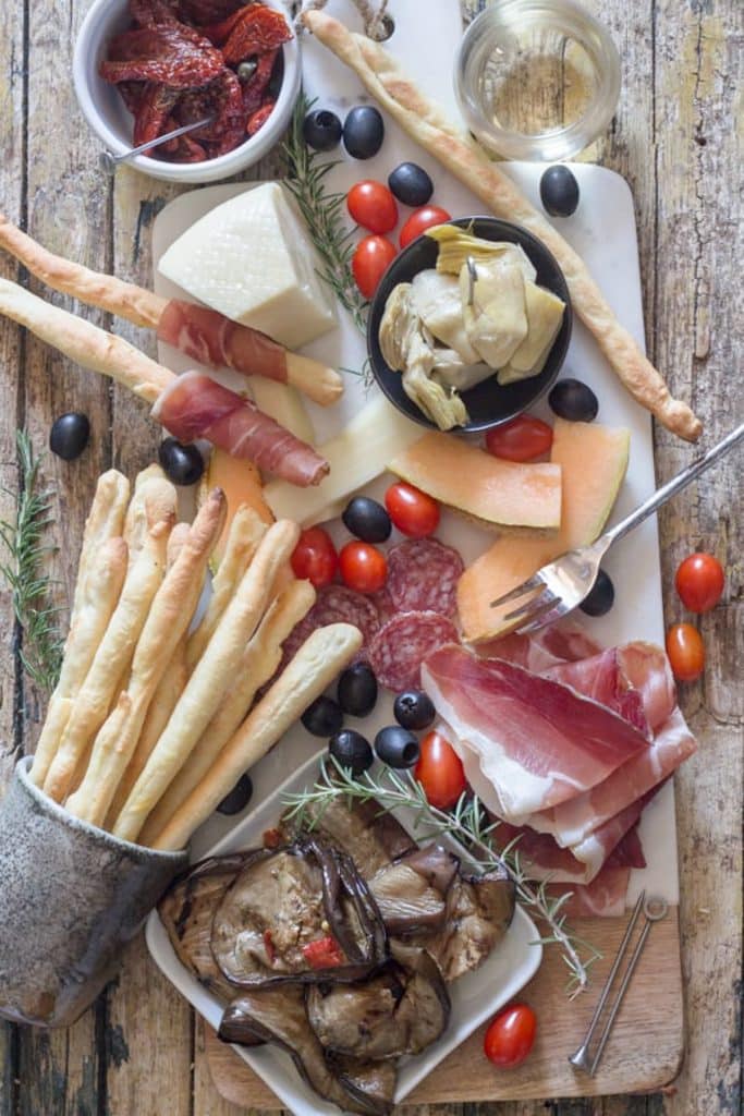 Grissini with cold meat, olives, artichokes on a board.