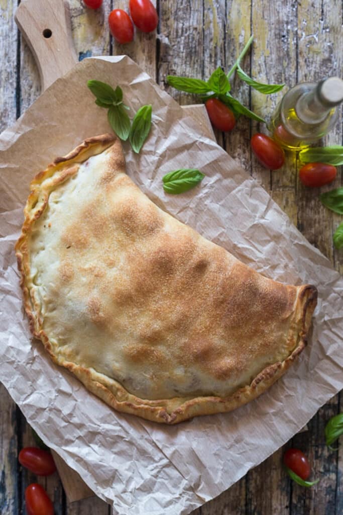Calzone on parchment paper with fresh tomatoes.