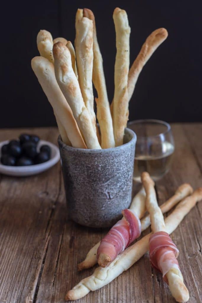 Breadsticks in a glass and 3 on the board with prosciutto.