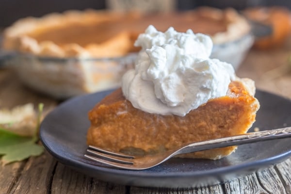 slice of pumpkin pie and maple whipped cream on a black plate