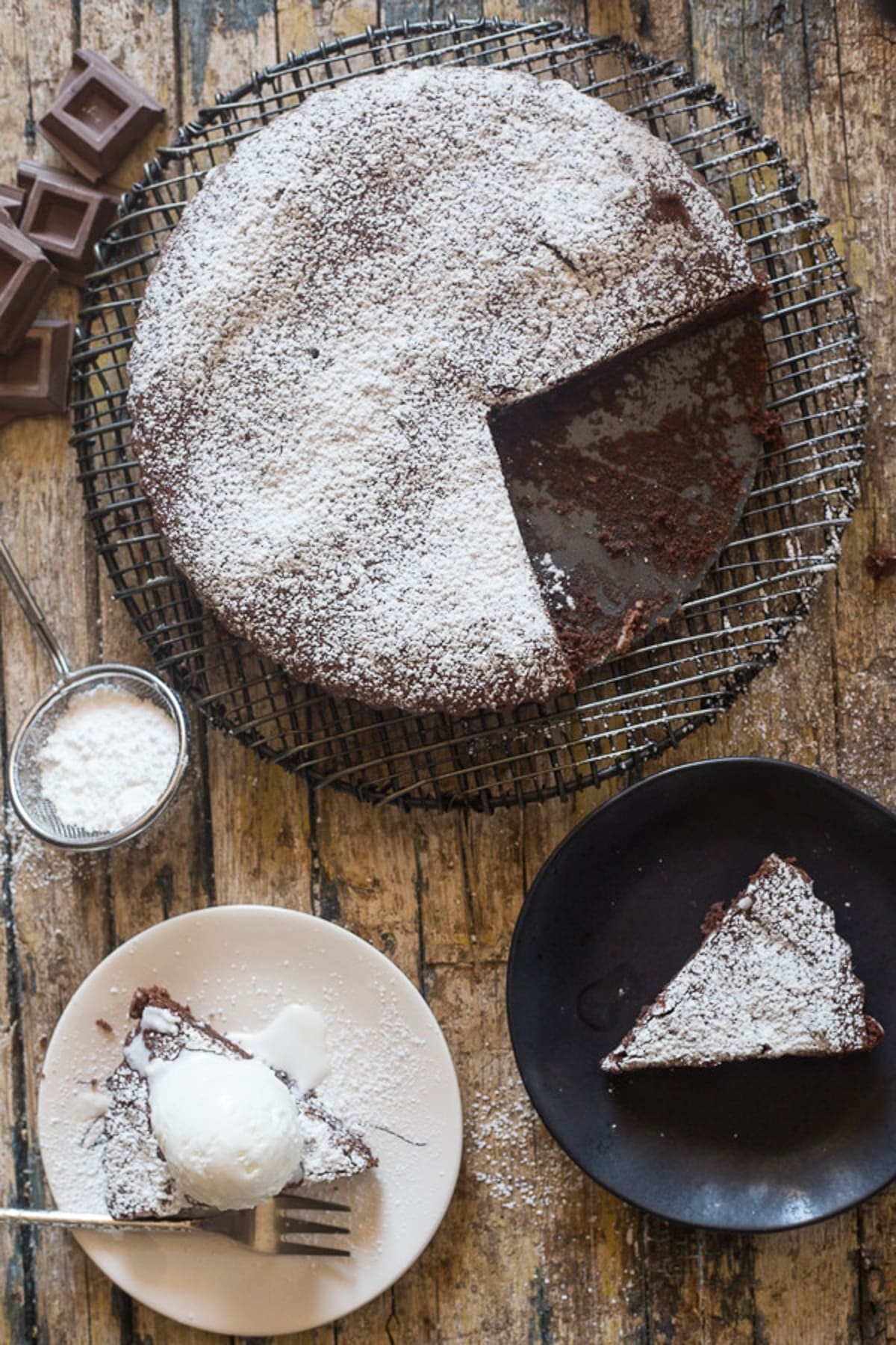 Cake on a wire rack and two pieces one on a black plate and one on a white plate.