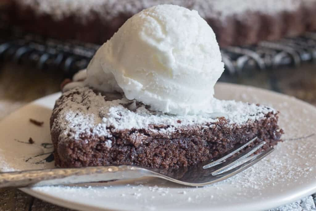 Brownie cake slice with a scoop of vanilla ice cream on a white plate.