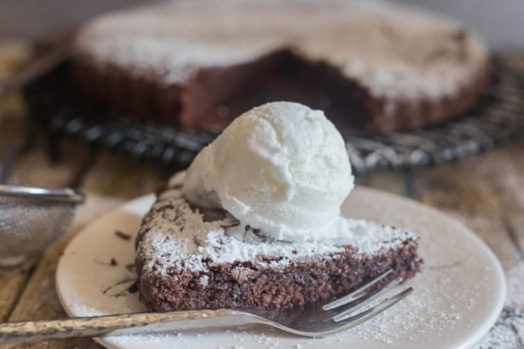 Brownie cake slice with a scoop of vanilla ice cream on a white plate.