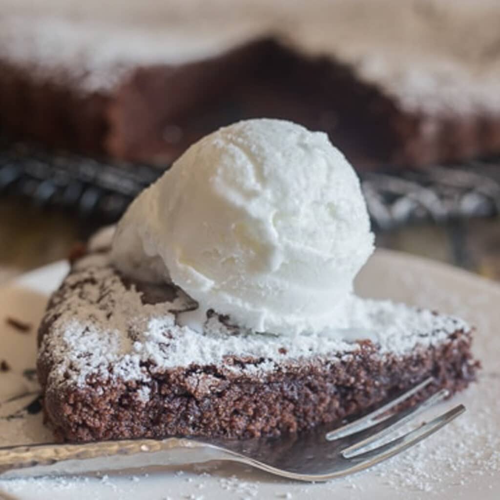 Brownie cake slice with a scoop of vanilla ice cream on a white plate.