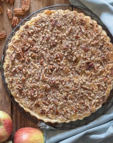Apple crostata on wooden board with apples and pecans.