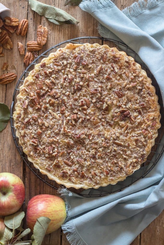 Apple crostata on wooden board with apples and pecans.
