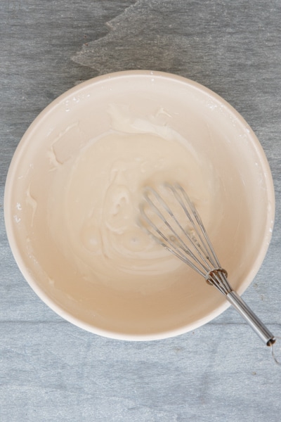 The maple glaze in a white bowl with a whisk.
